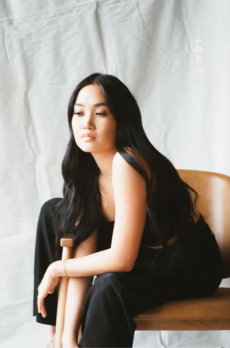 A girl wearing all black, sitting in front of a white backdrop in a brown chair. Shot on 35mm film.