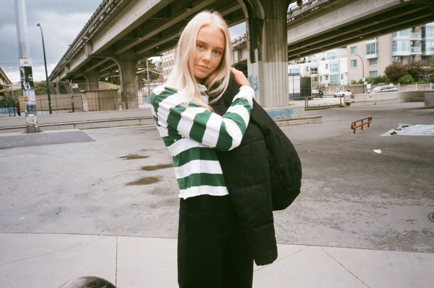 A girl in a green and white stripped polo shirt posing in a skate park. Shot on 35mm film.