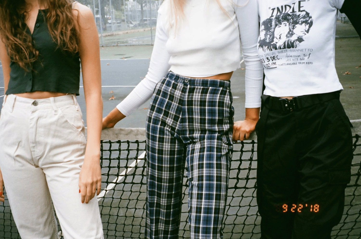 Three girls posing in front of a tennis court net. Shot on 35mm film.